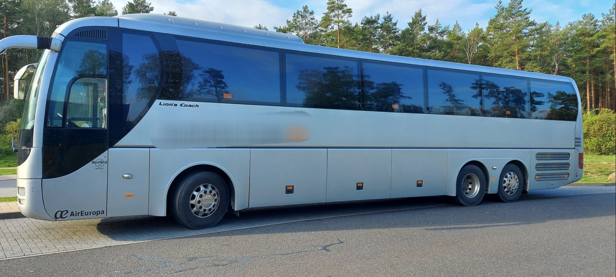 Srebrny autokar Lion's Coach z logo AirEuropa zaparkowany na parkingu, z widocznymi drzewami w tle odbijającymi się w oknach.