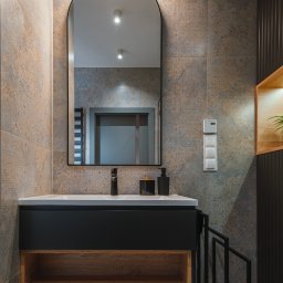 Project-art - Nowoczesna łazienka z umywalką nablatową, czarną armaturą i lustrem w kształcie łuku, podświetlonym od góry, na tle płytek w odcieniach szarości i beżu z delikatnym wzorem.