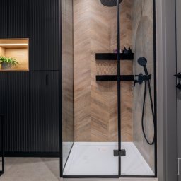 Project-art - Nowoczesna łazienka z kabiną prysznicową typu walk-in, wykończona płytkami w jodełkę, czarnymi meblami z ryflowanymi frontami i oświetloną wnęką z rośliną.