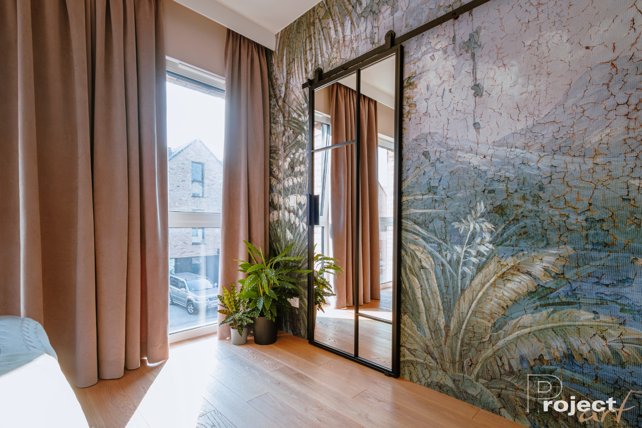 Pokój z przesuwnymi lustrzanymi drzwiami na szynie, roślinami doniczkowymi przy oknie z beżowymi zasłonami i tapetą w stylu vintage z motywem roślinnym.