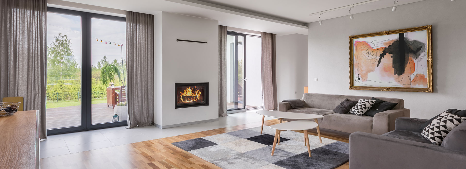 Jasne wnętrze salonu z kominkiem, sofą i widokiem na taras z ogrodem przez duże okna.