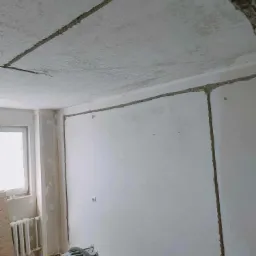 Przygotowanie ścian i sufitu do położenia gładzi, widoczne wycięte szczeliny dylatacyjne oraz odkurzacz przemysłowy Karcher.