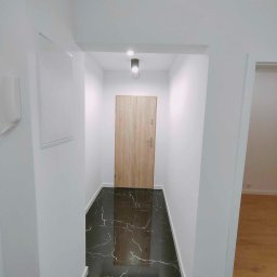 Przedsiębiorstwo Usługowe Jarosław Butowski - Nowoczesny korytarz z czarną, marmurkową podłogą, białymi ścianami i drewnianymi drzwiami wejściowymi, oświetlony punktowym światłem.