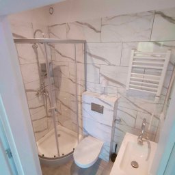 Przedsiębiorstwo Usługowe Jarosław Butowski - Nowoczesna łazienka z marmurowymi płytkami, kabiną prysznicową z chromowanymi elementami, podwieszaną toaletą i grzejnikiem drabinkowym.