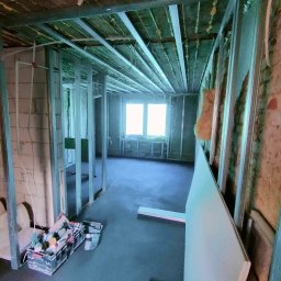 Przedsiębiorstwo Usługowe Jarosław Butowski - Wnętrze w trakcie remontu: widoczne metalowe profile konstrukcyjne ścian i sufitu, izolacja w suficie, surowy beton na podłodze, skrzynka z narzędziami i płyta karton gips