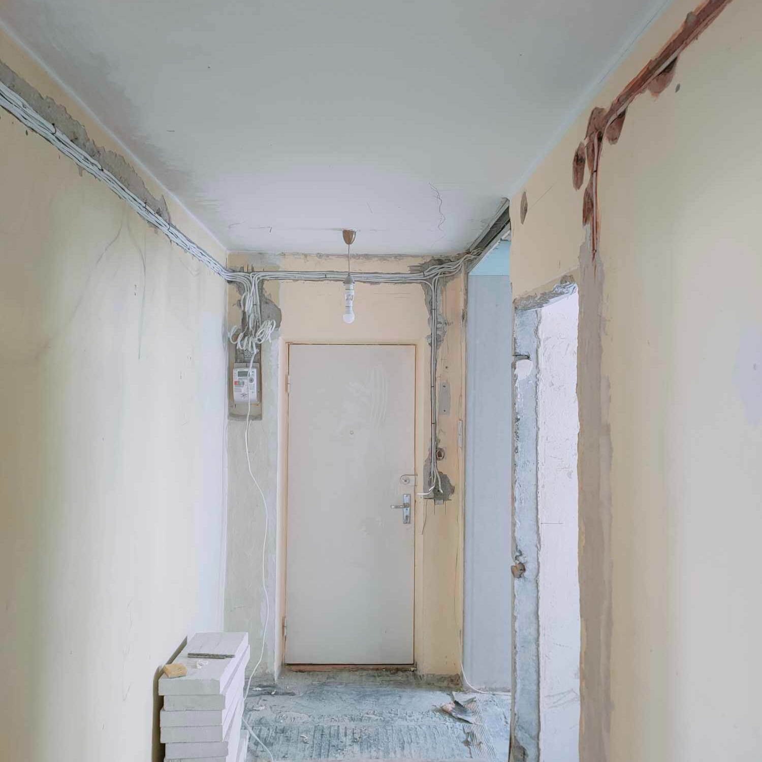 Korytarz w trakcie prac remontowych: widoczne przewody elektryczne prowadzone po ścianach, przygotowane bloczki z betonu komórkowego i surowy otwór drzwiowy obok wejścia.