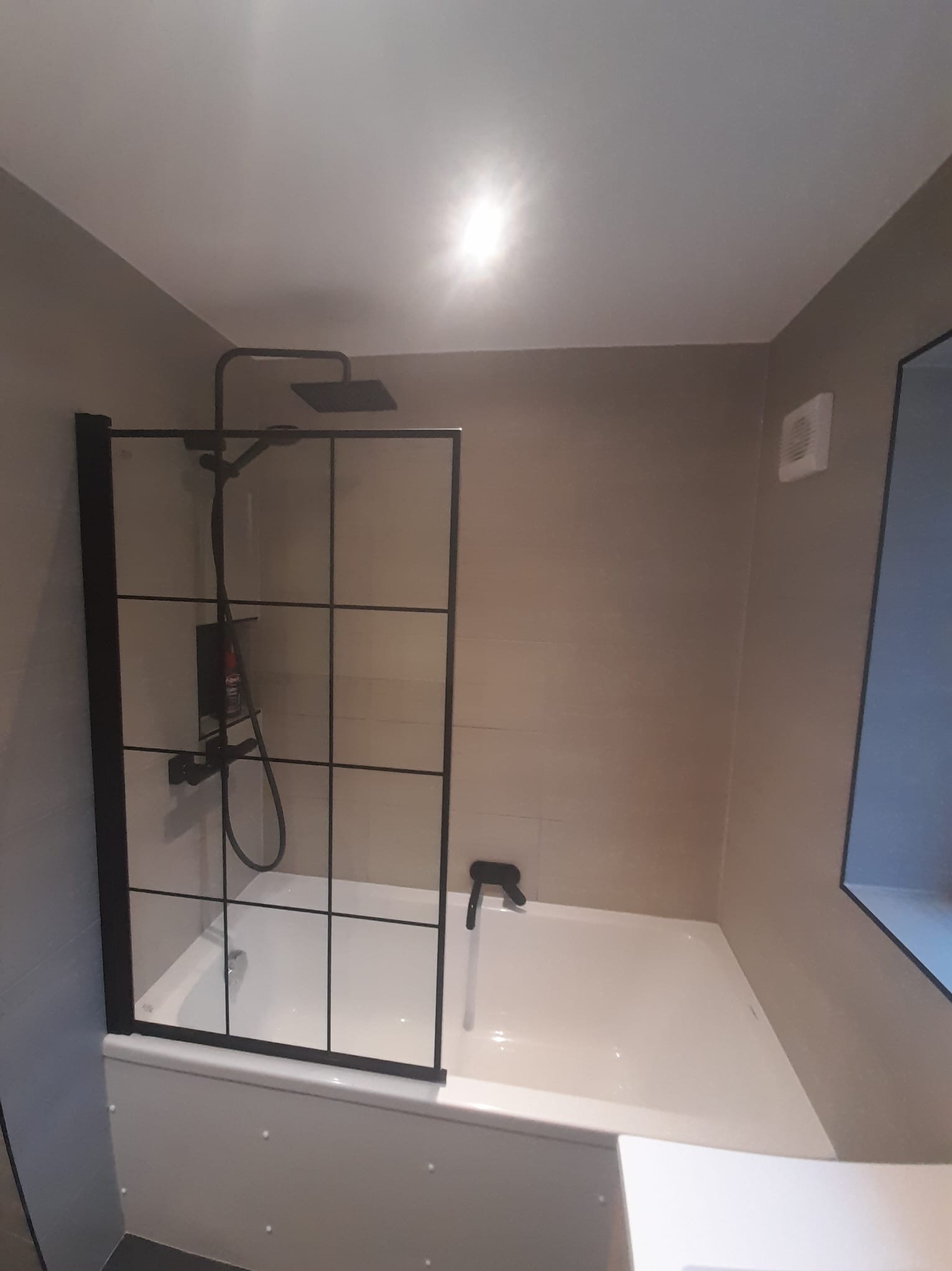 Nowoczesna kabina prysznicowa z czarną ramą i deszczownicą w łazience z beżowymi płytkami.