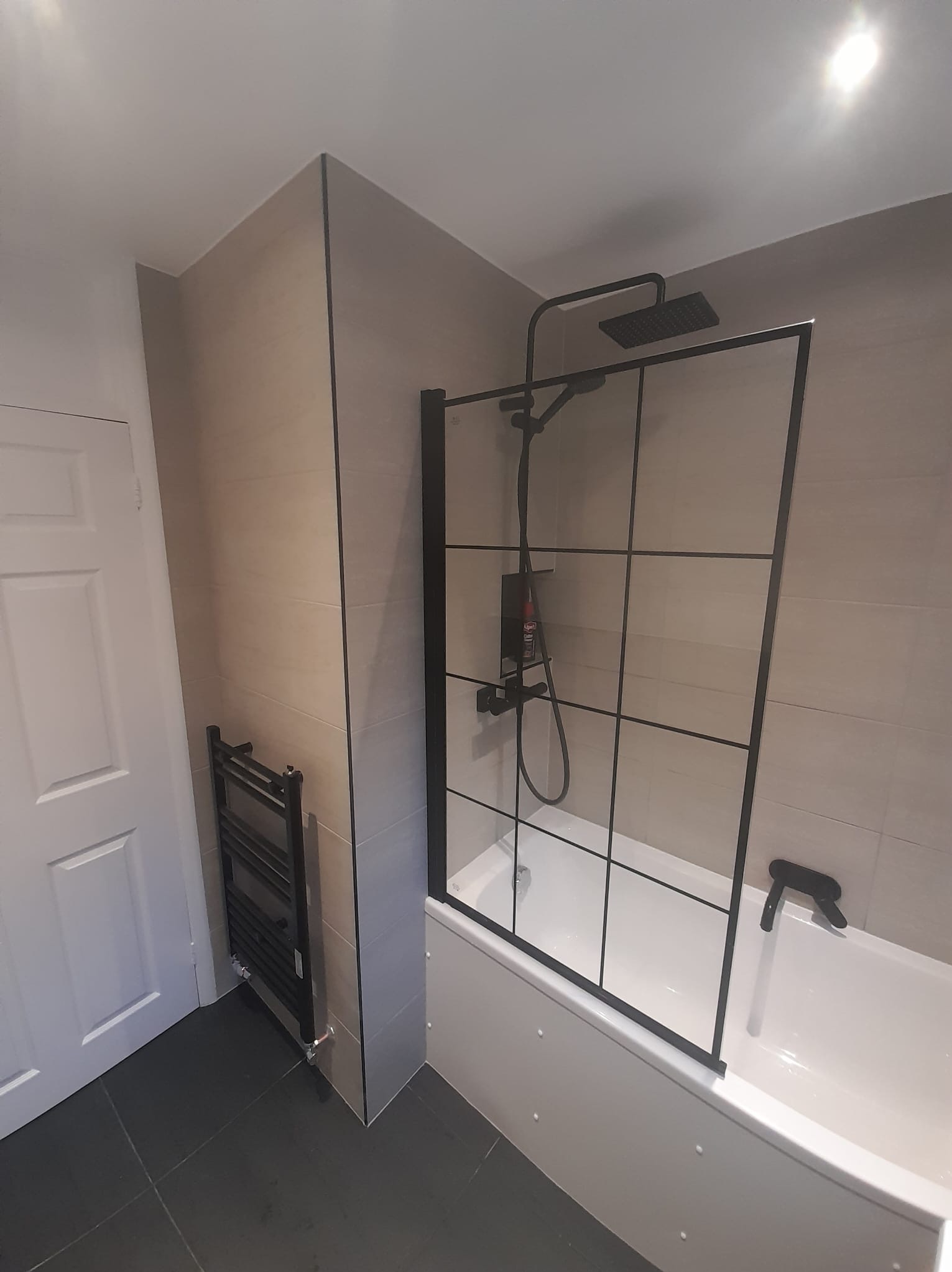 Wyremontowana łazienka z kabiną prysznicową typu walk-in z czarnymi profilami, grzejnikiem drabinkowym i szarą glazurą.