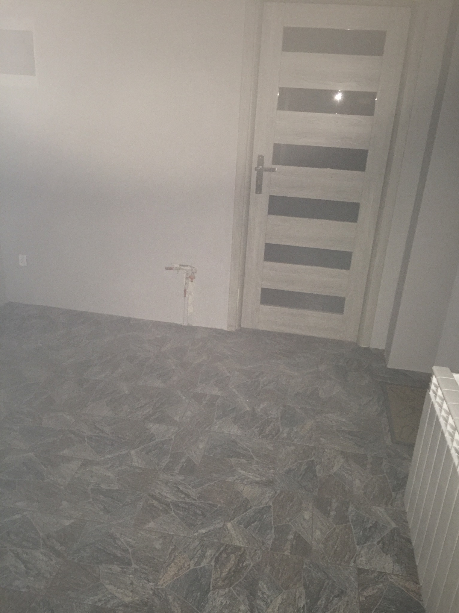 Szare płytki podłogowe imitujące kamień w łazience, widoczna biała, panelowa drzwi i fragment grzejnika.