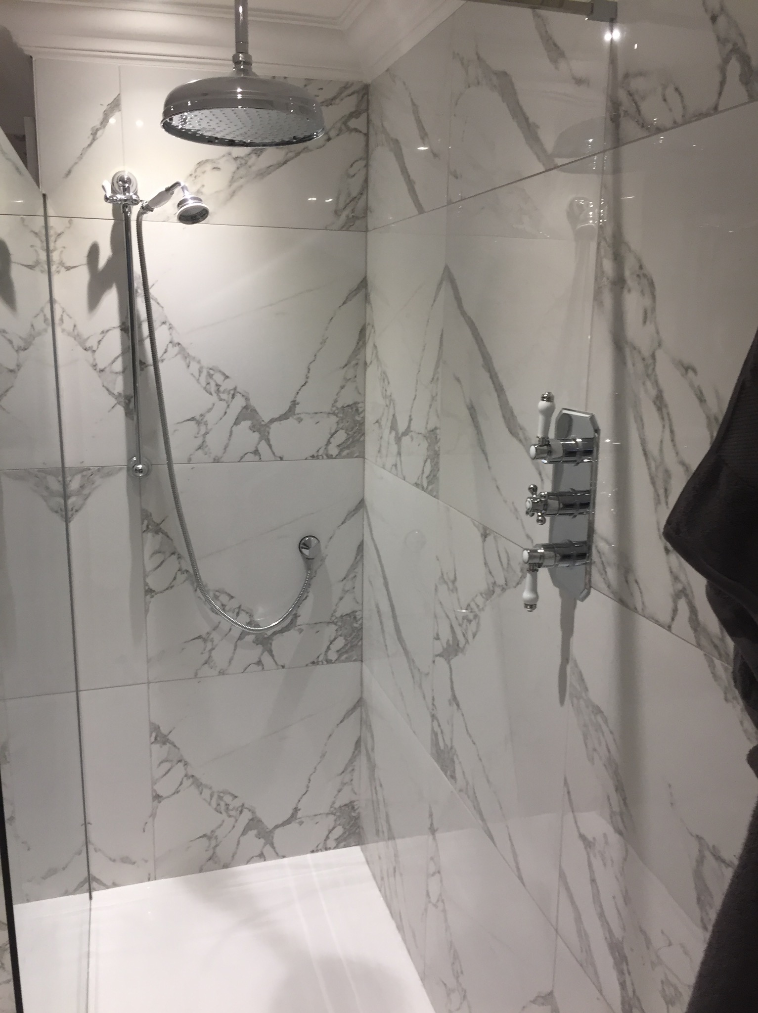 Nowoczesna kabina prysznicowa z deszczownicą i baterią retro, wykończona białymi płytkami imitującymi marmur.