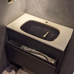 Fabryka Mebli Farmahei - Montaż szafki łazienkowej z blatem w Warszawie, widoczne podłączenia hydrauliczne i otwarte gniazdka elektryczne w ścianie.