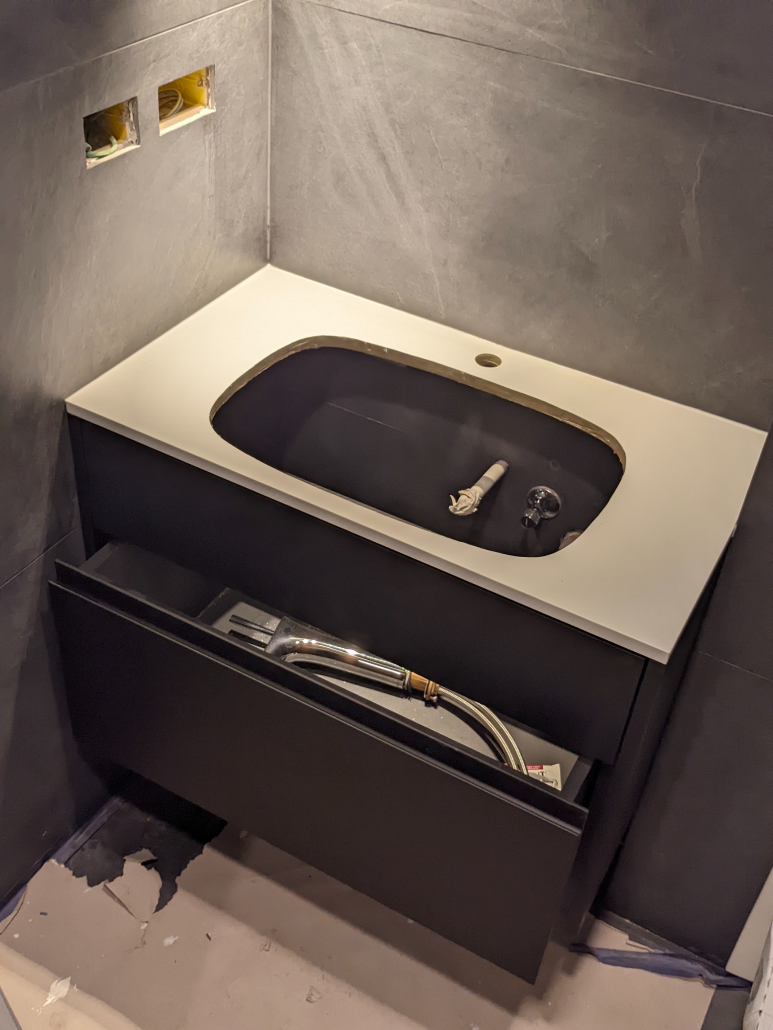 Montaż szafki łazienkowej z blatem w Warszawie, widoczne podłączenia hydrauliczne i otwarte gniazdka elektryczne w ścianie.