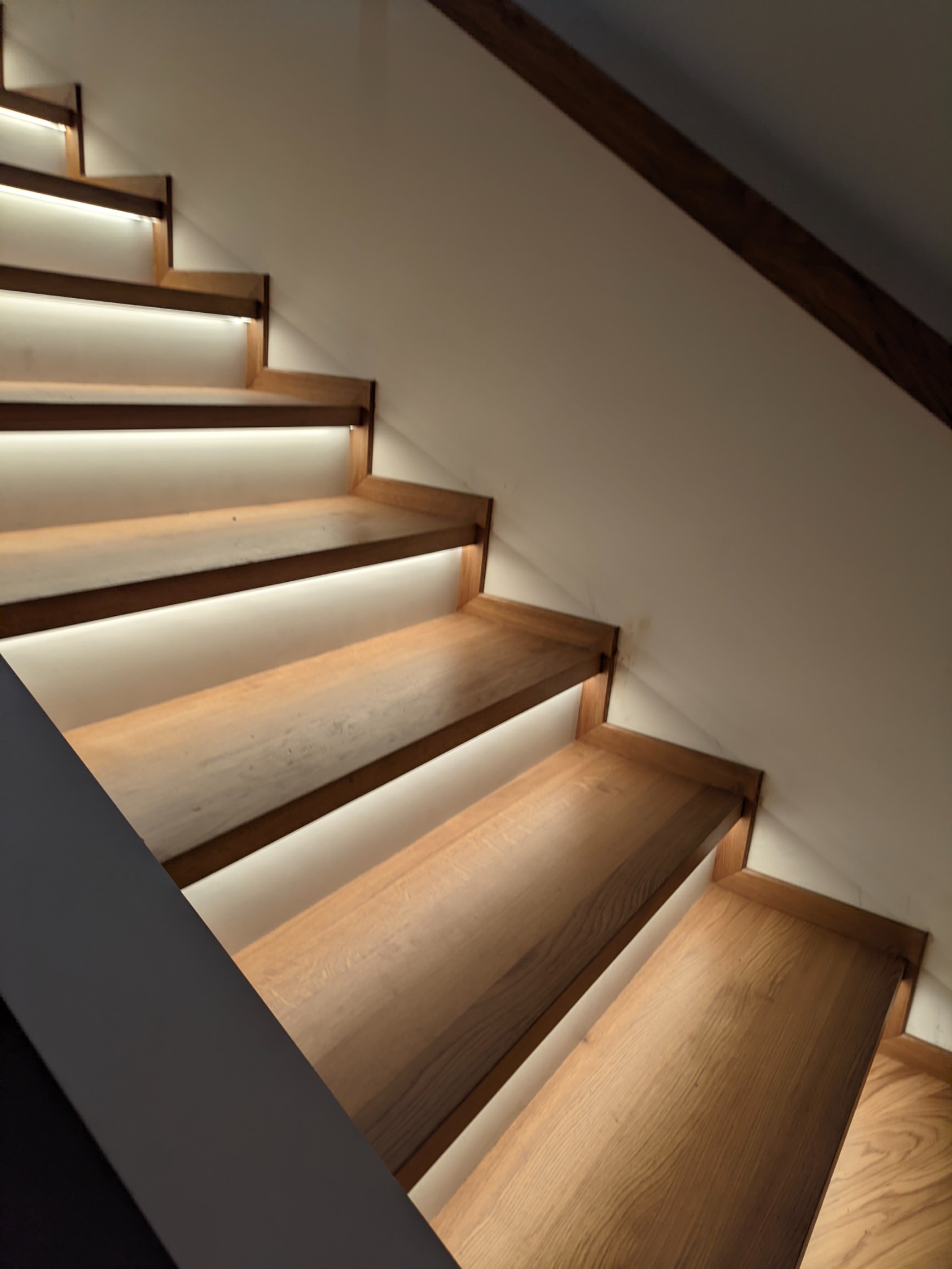 Drewniane schody z podświetleniem LED, widok z dołu, nowoczesny design, jasne drewno, minimalistyczne wykończenie.