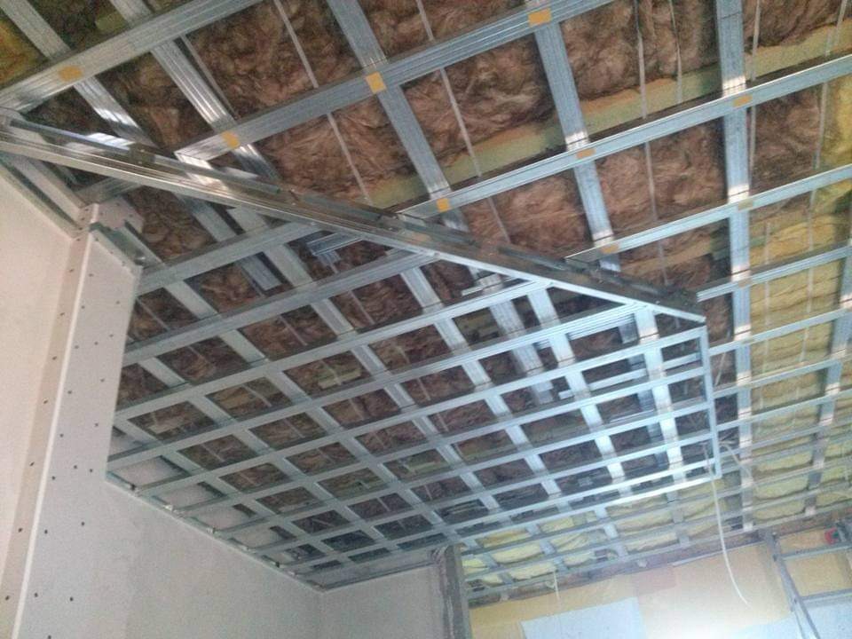 Metalowa konstrukcja sufitu podwieszanego z izolacją z wełny mineralnej, widok z dołu, etap montażu.