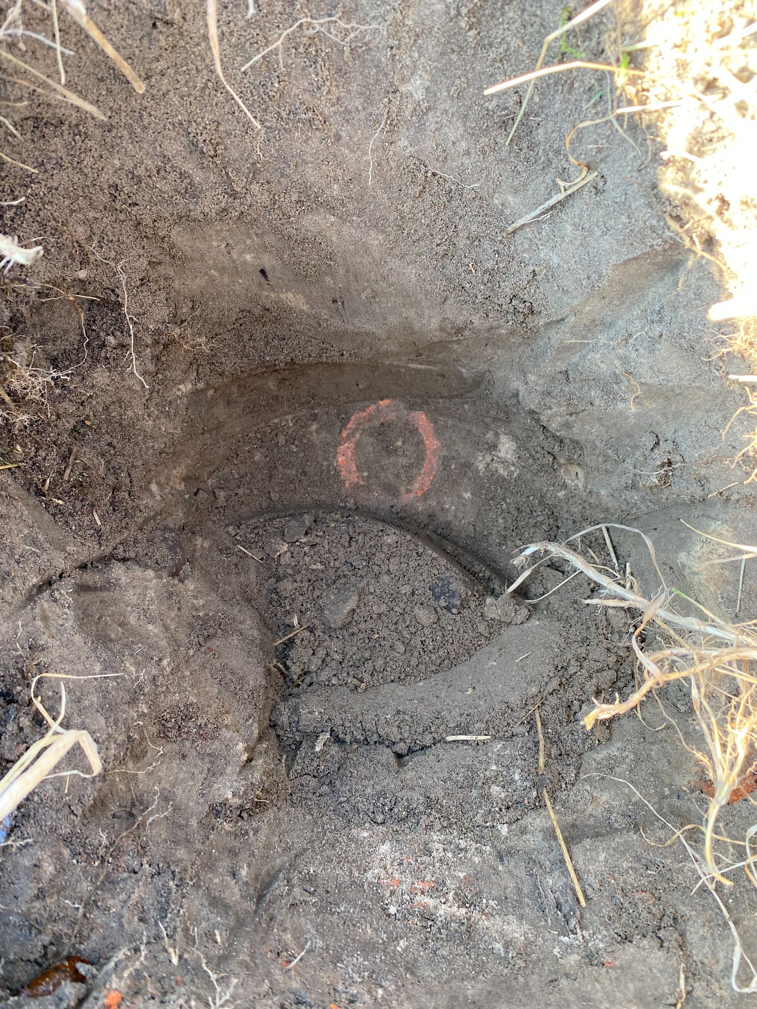 Wykonany wykop z widoczną pomarańczową obręczą wyznaczającą punkt pomiarowy w ziemi, z suchą trawą na krawędzi.