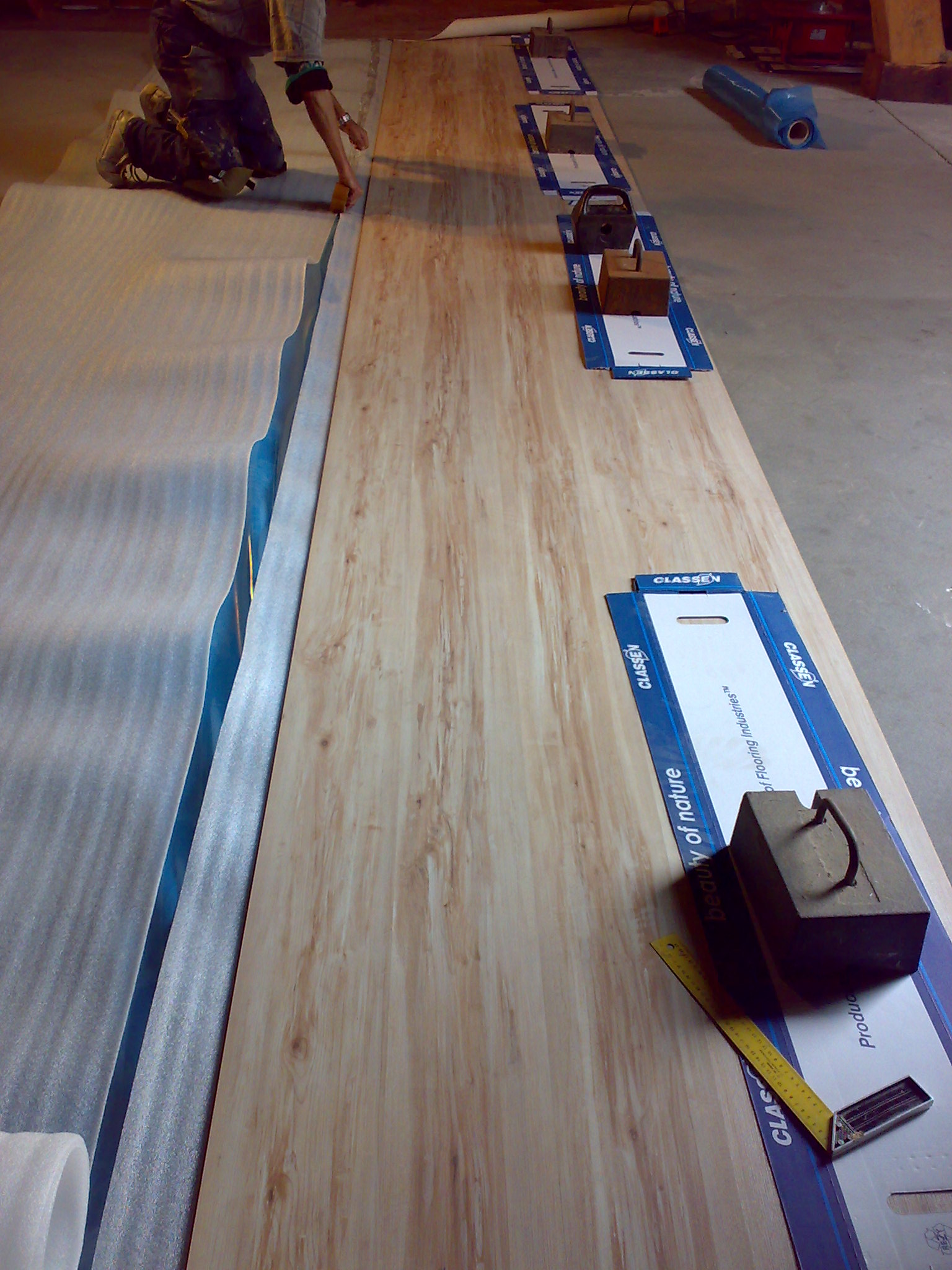 Montaż paneli: pracownik docina piankę podkładową przy użyciu noża, obok ułożone narzędzia i ciężarki na kartonowych podkładkach marki Classen.