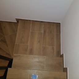DZIKU Uslugi Remontowo-Wykonczeniowe Tomasz Gorzel - Ułożone brązowe płytki imitujące drewno na schodach, widok z góry, mała puszka z farbą na jednym ze stopni.