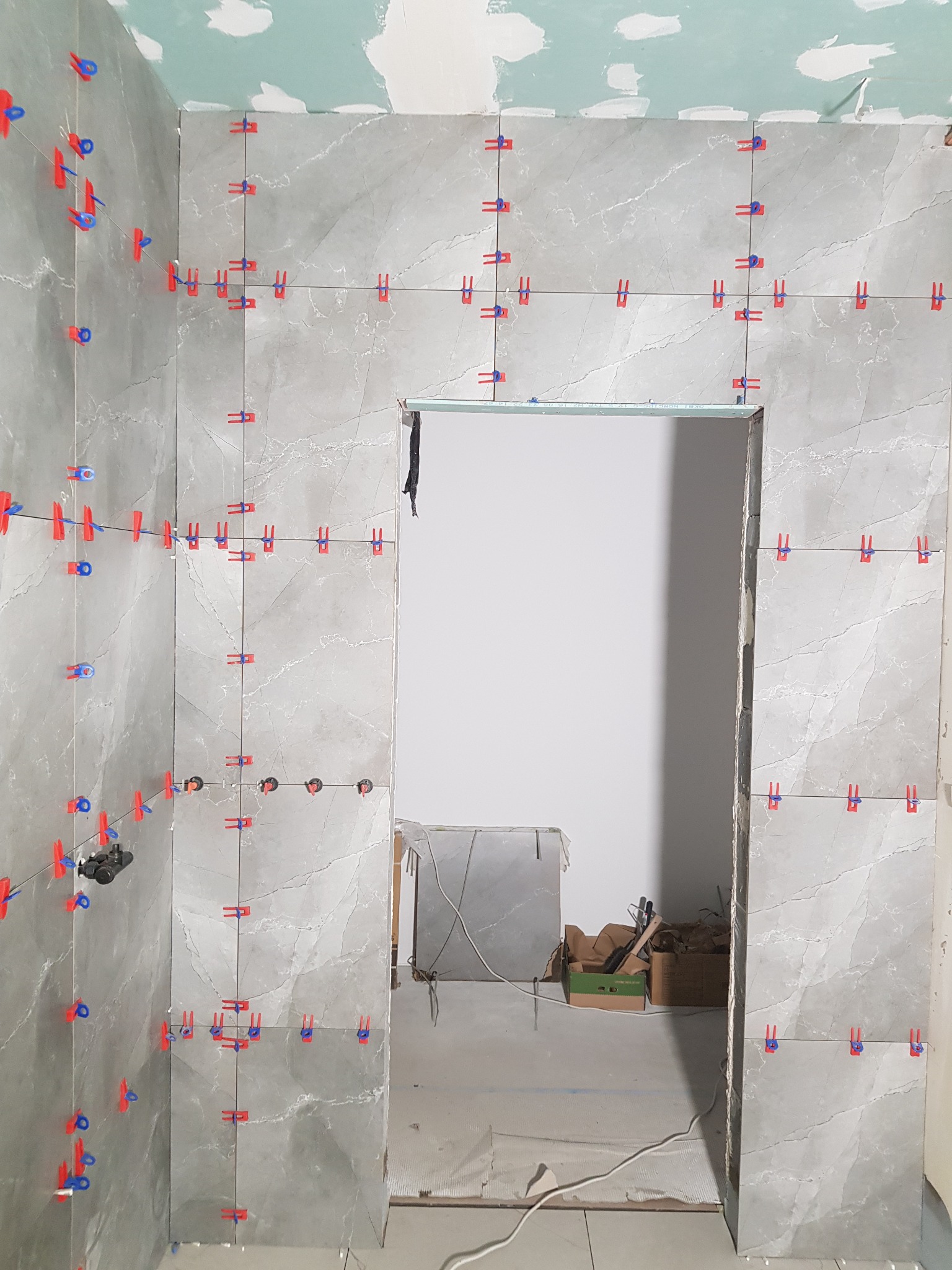 Układanie szarych płytek imitujących marmur z użyciem klipsów poziomujących w trakcie prac. Widoczne narzędzia i materiały budowlane w tle.