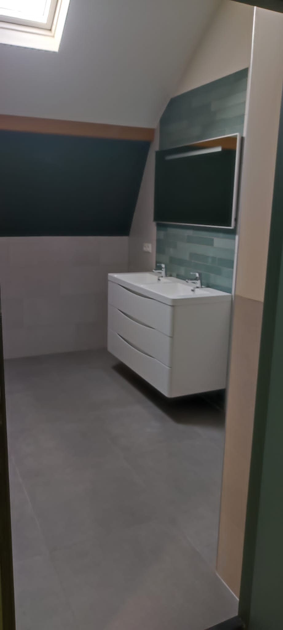 Ukończona łazienka na poddaszu ze skośnym sufitem, biała szafka z umywalkami i lustro na ścianie z turkusową mozaiką.