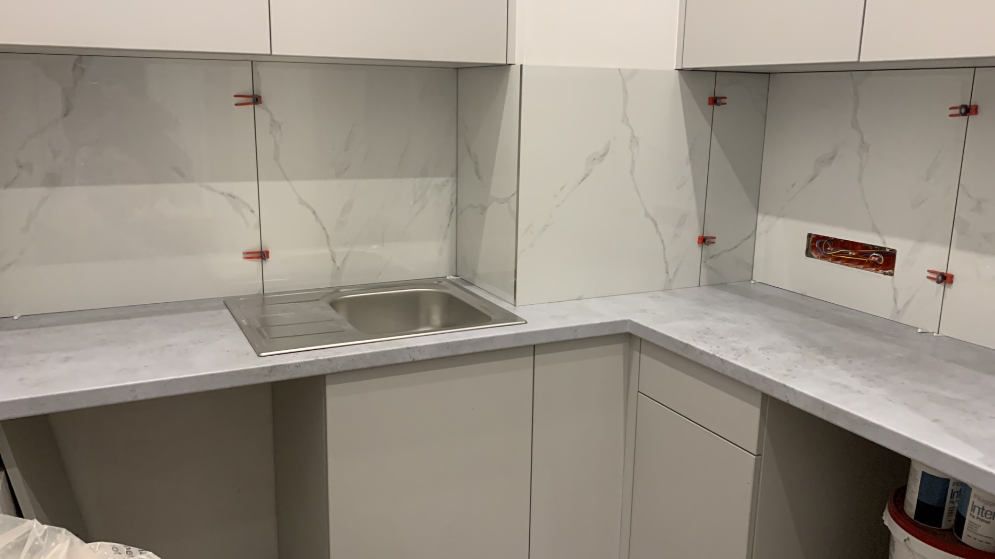 Montaż płytek imitujących marmur na ścianie nad zlewem w kuchni, widoczne krzyżyki dystansowe i otwór na gniazdko elektryczne.