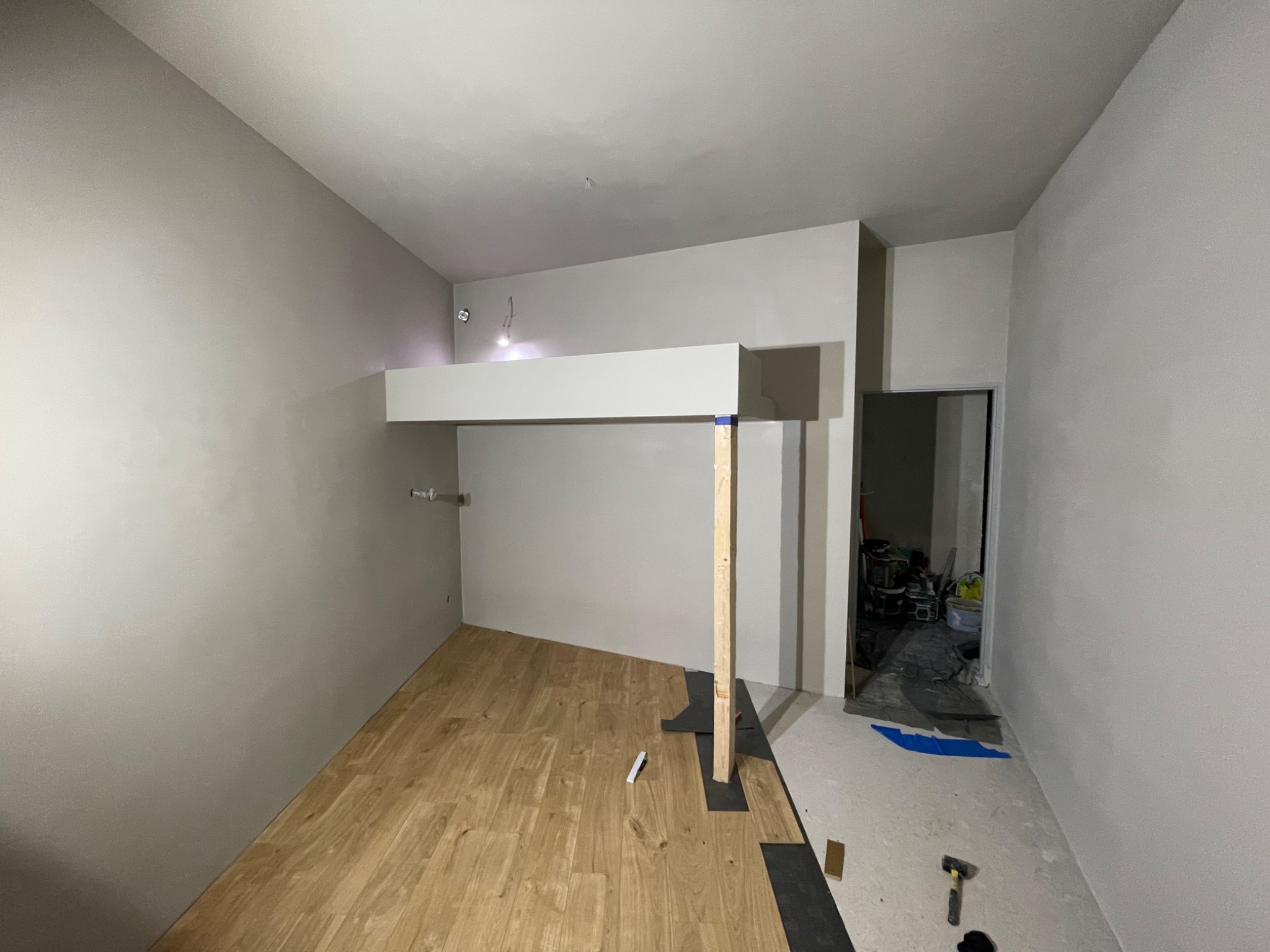 Wnętrze w trakcie remontu: częściowo ułożona podłoga z paneli, surowe ściany przygotowane do malowania, widoczne narzędzia i materiały budowlane.