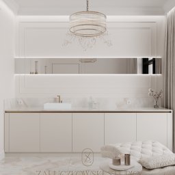 Załuczkowski Studio Interior Architecture - Elegancka łazienka w odcieniach beżu i bieli, z marmurową podłogą, szafką pod umywalką z białym blatem, lustrem z oświetleniem LED, ozdobnym żyrandolem, i fotelem z małym stolikiem kawowym.