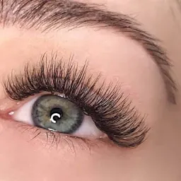 Zbliżenie na oko z zieloną tęczówką i perfekcyjnie przedłużonymi, gęstymi rzęsami w stylu 'kocie oko', z widoczną, naturalną brwią.