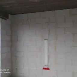 Surowy stan wnętrza w trakcie prac elektrycznych: widoczne przewody elektryczne prowadzone po ścianie z betonu komórkowego, puszki instalacyjne w kolorze czerwonym oraz niezabezpieczone okno...