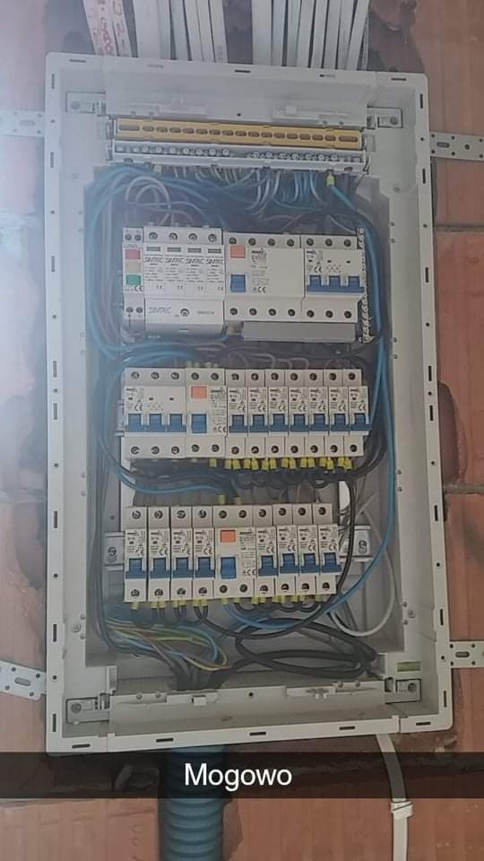 Otwarta skrzynka rozdzielcza z licznymi bezpiecznikami i przewodami, zamontowana na ścianie z cegły.