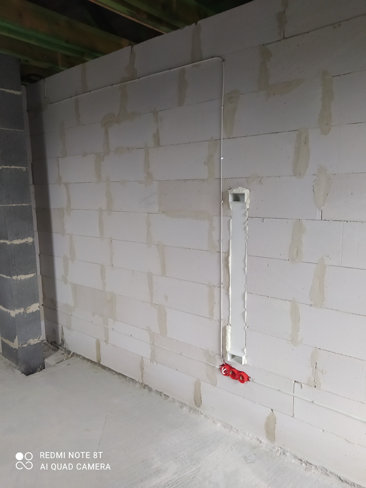 Ściana z betonu komórkowego z pionowym kanałem instalacyjnym wypełnionym pianką montażową i przymocowanym przewodem elektrycznym w czerwonych uchwytach.