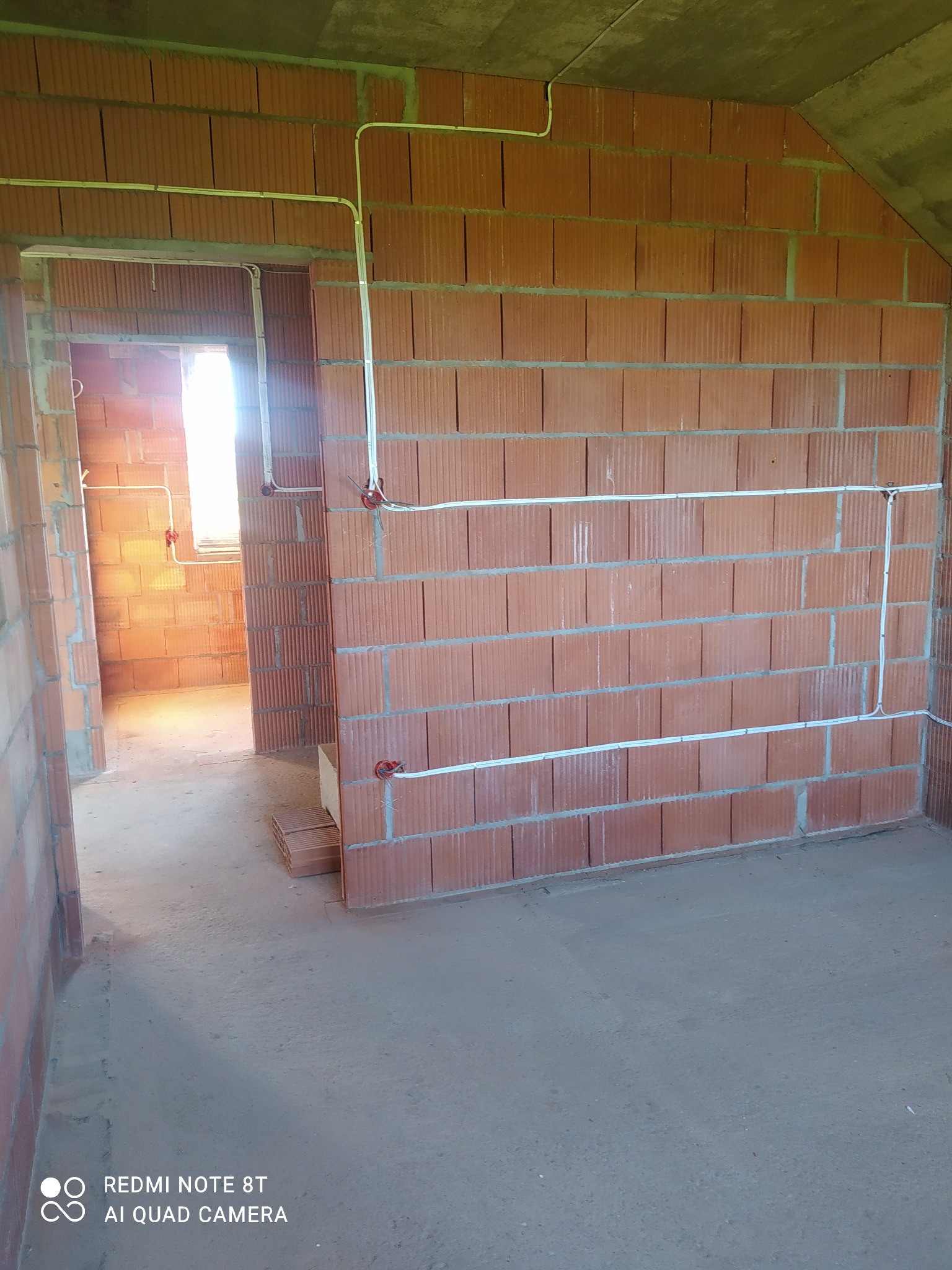 Surowy stan: Instalacja przewodów elektrycznych natynkowych w nowo wzniesionym budynku z cegły ceramicznej dziurawki, widoczne puszki instalacyjne i fragment stropu.