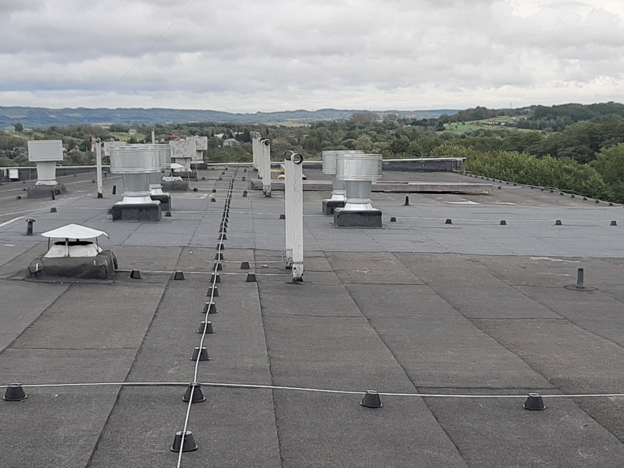 Wykończony dach hali przemysłowej w Międzyrzecu Podlaskim z widocznymi systemami wentylacyjnymi i zabezpieczeniami przeciwśniegowymi na tle zielonych wzgórz.