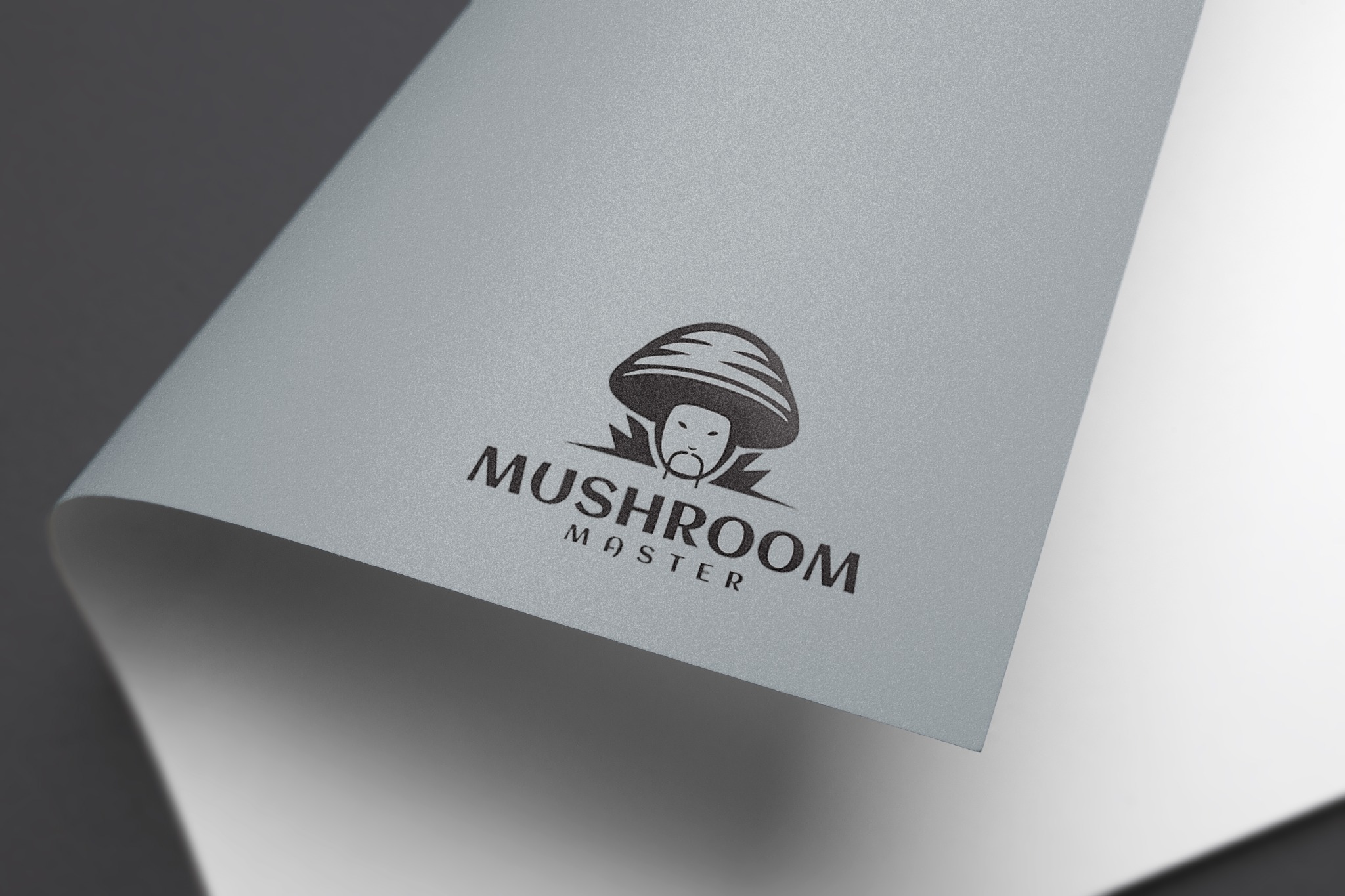 Logo Mushroom Master wydrukowane na teksturowanym, srebrnym papierze z zakręconym rogiem, na ciemnoszarym tle.