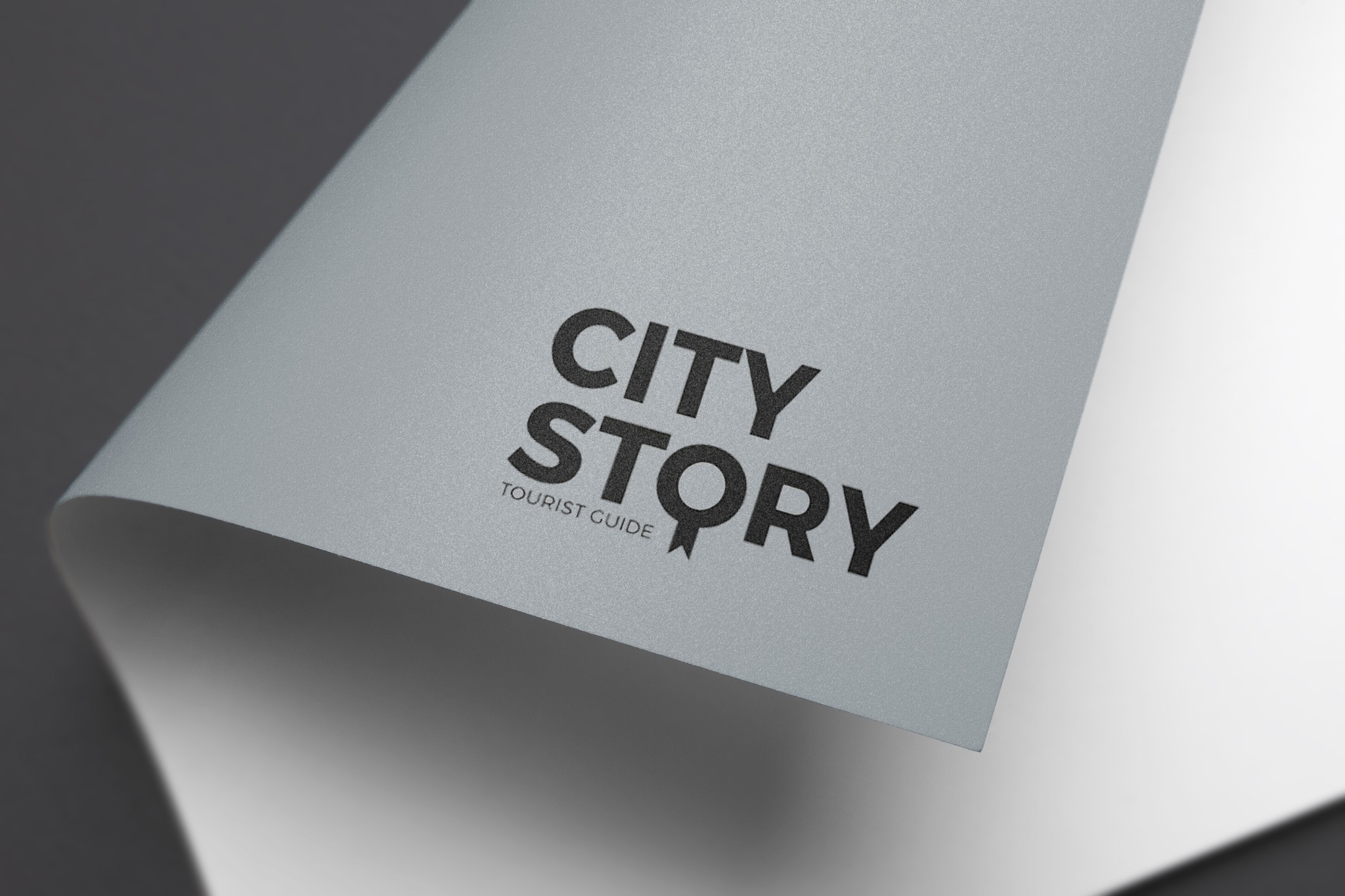 Elegancko wygięta kartka z logo 'City Story Tourist Guide' w czerni na szarym teksturowanym tle.