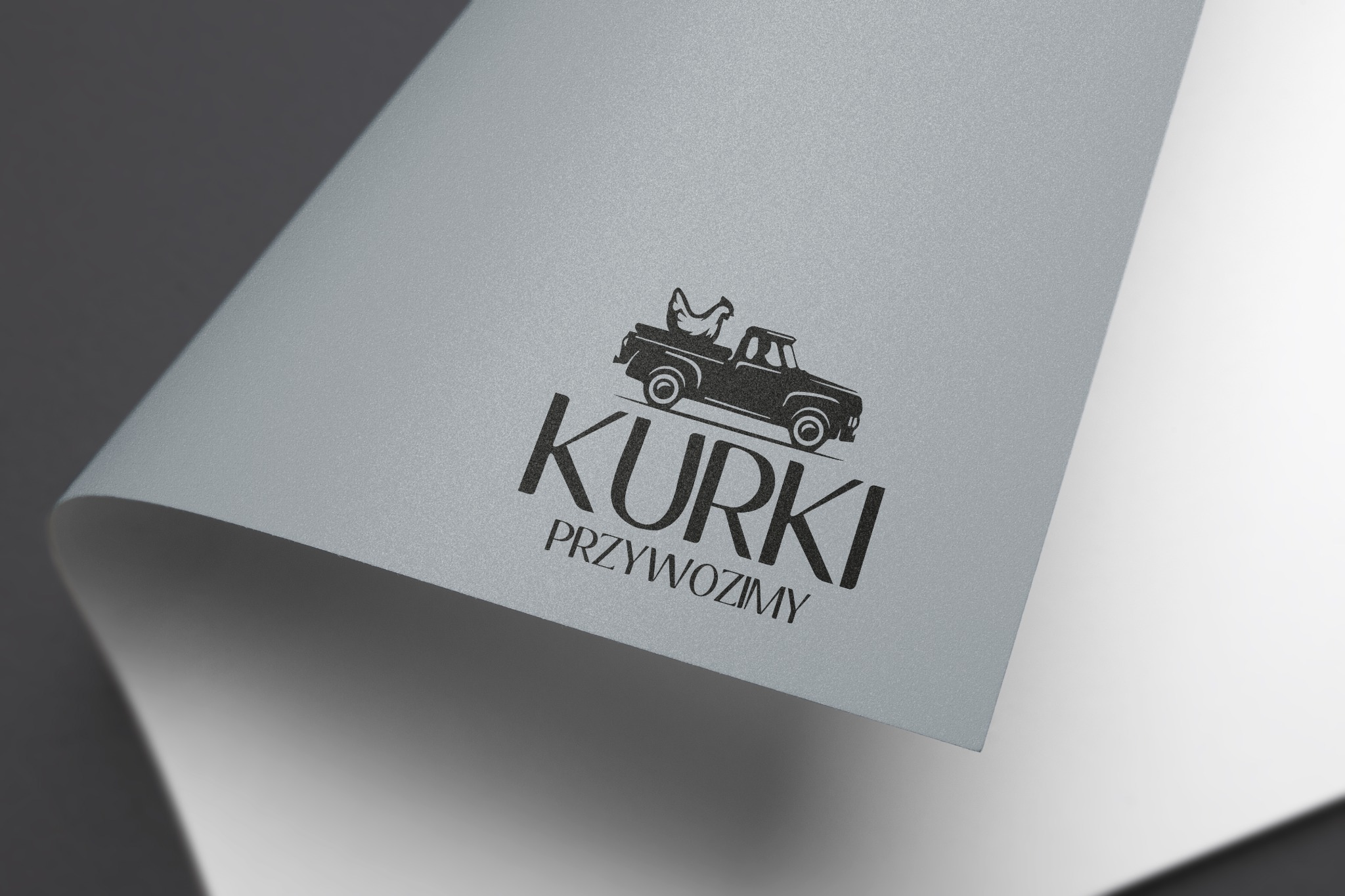 Eleganckie logo 'Kurki Przywozimy' w czerni, przedstawiające kurę w pickupie, umieszczone na srebrzystoszarym papierze z subtelnym efektem zwijania, na dwubarwnym szarym tle.