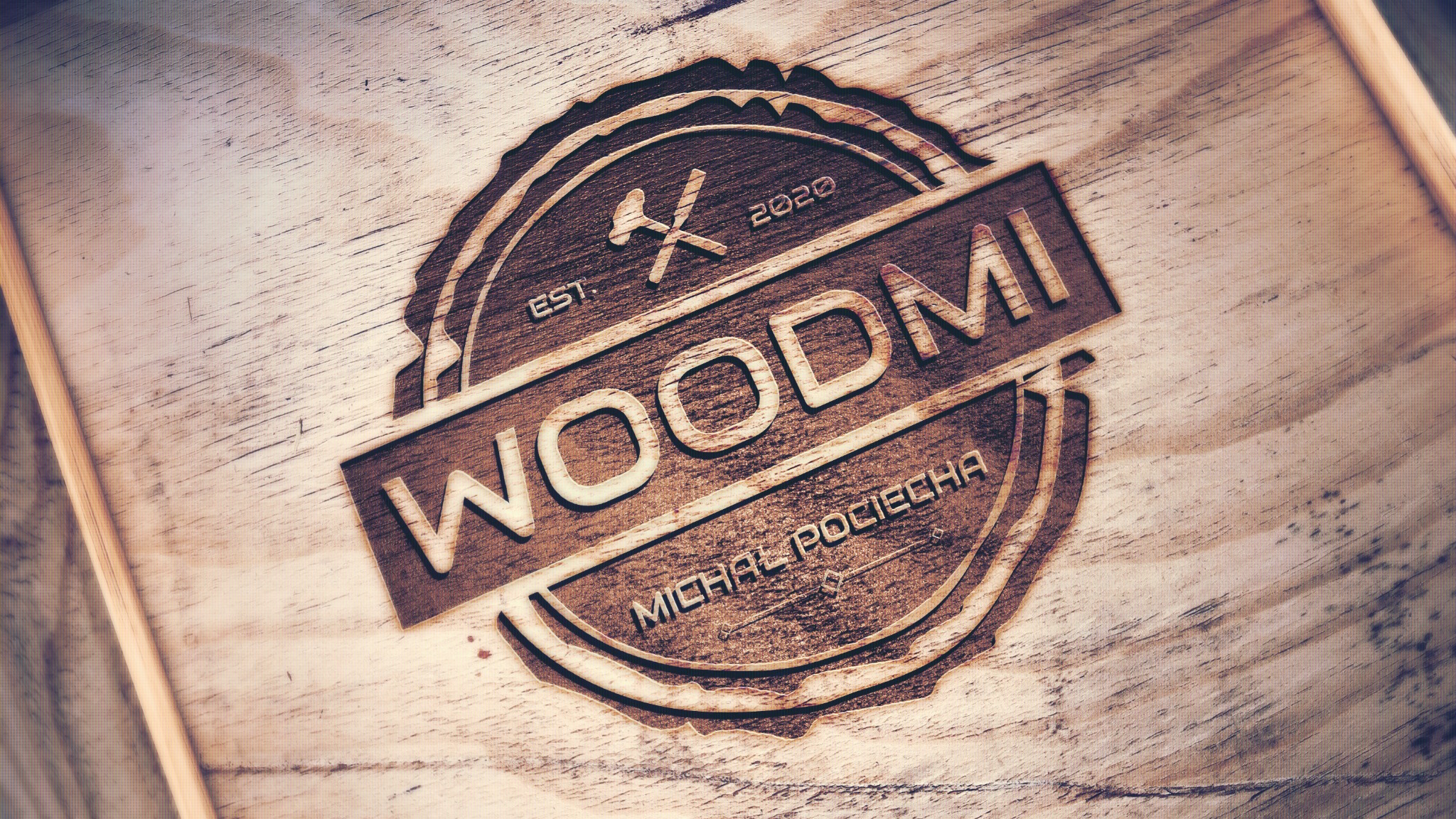 Wyżłobione logo firmy WOODMI na drewnianej desce, z datą EST. 2020 i imieniem projektanta Michał Pociecha, z motywem skrzyżowanego młotka i piły w okrągłej ramie.