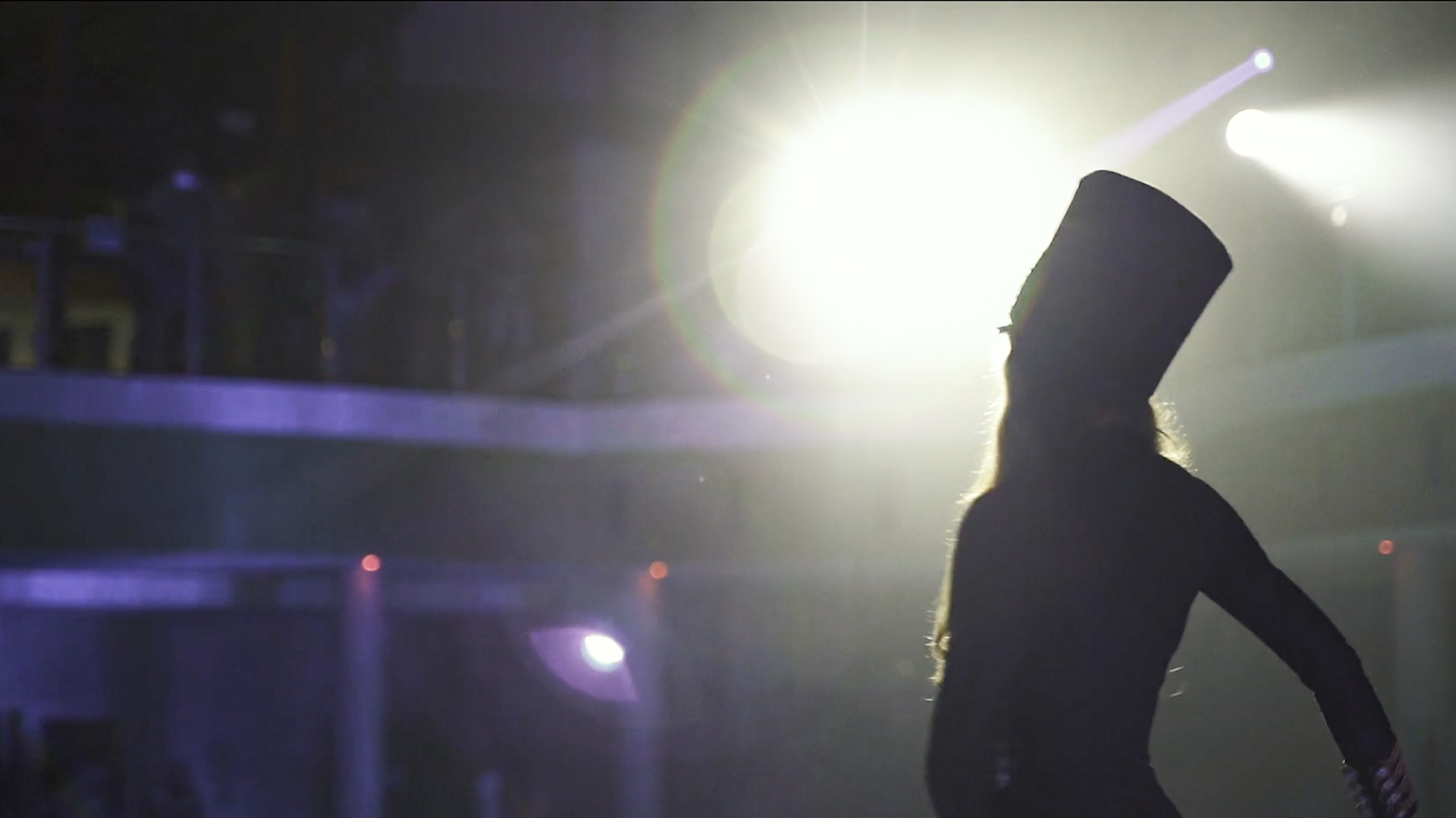 Sylwetka osoby w wysokim cylindrze na scenie w Krakowie, oświetlona reflektorami, widoczna balustrada balkonu.