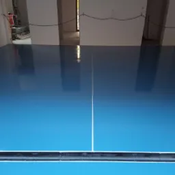 Błękitna, błyszcząca posadzka w pomieszczeniu w trakcie wykańczania, widoczna listwa przypodłogowa i surowe wnętrze w tle.