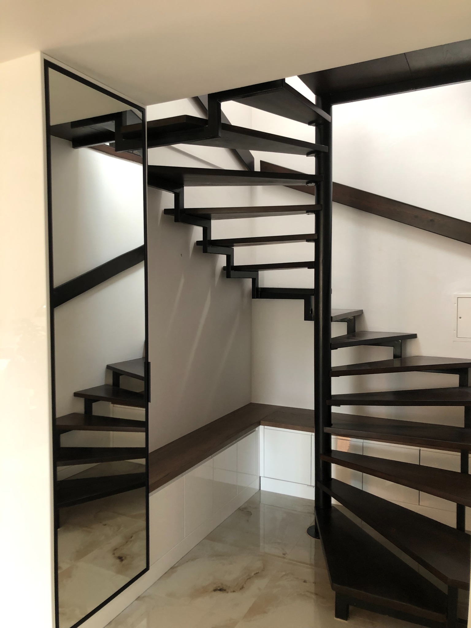 Spiralne schody drewniane z czarną metalową konstrukcją, widoczne z dołu, obok zabudowa z siedziskiem i lustrem.