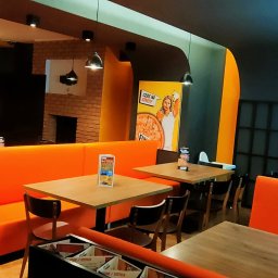 Speedy Romano - Wnętrze pizzerii z pomarańczowymi kanapami, drewnianymi stolikami i krzesłami, dekoracjami ściennymi z motywem pizzy i balonami.