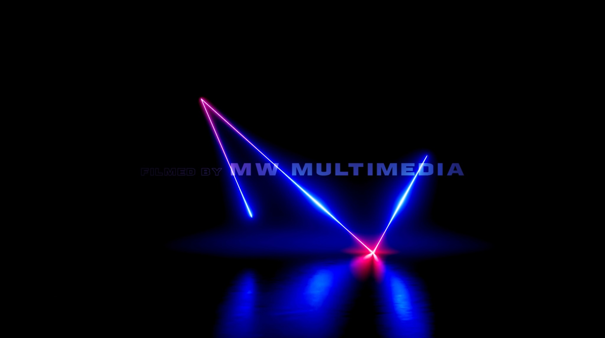 Abstrakcyjne zdjęcie z neonowymi liniami w kolorach różu i błękitu, odbijającymi się w ciemnej powierzchni. Widoczny napis 'FILMED BY MW MULTIMEDIA'.