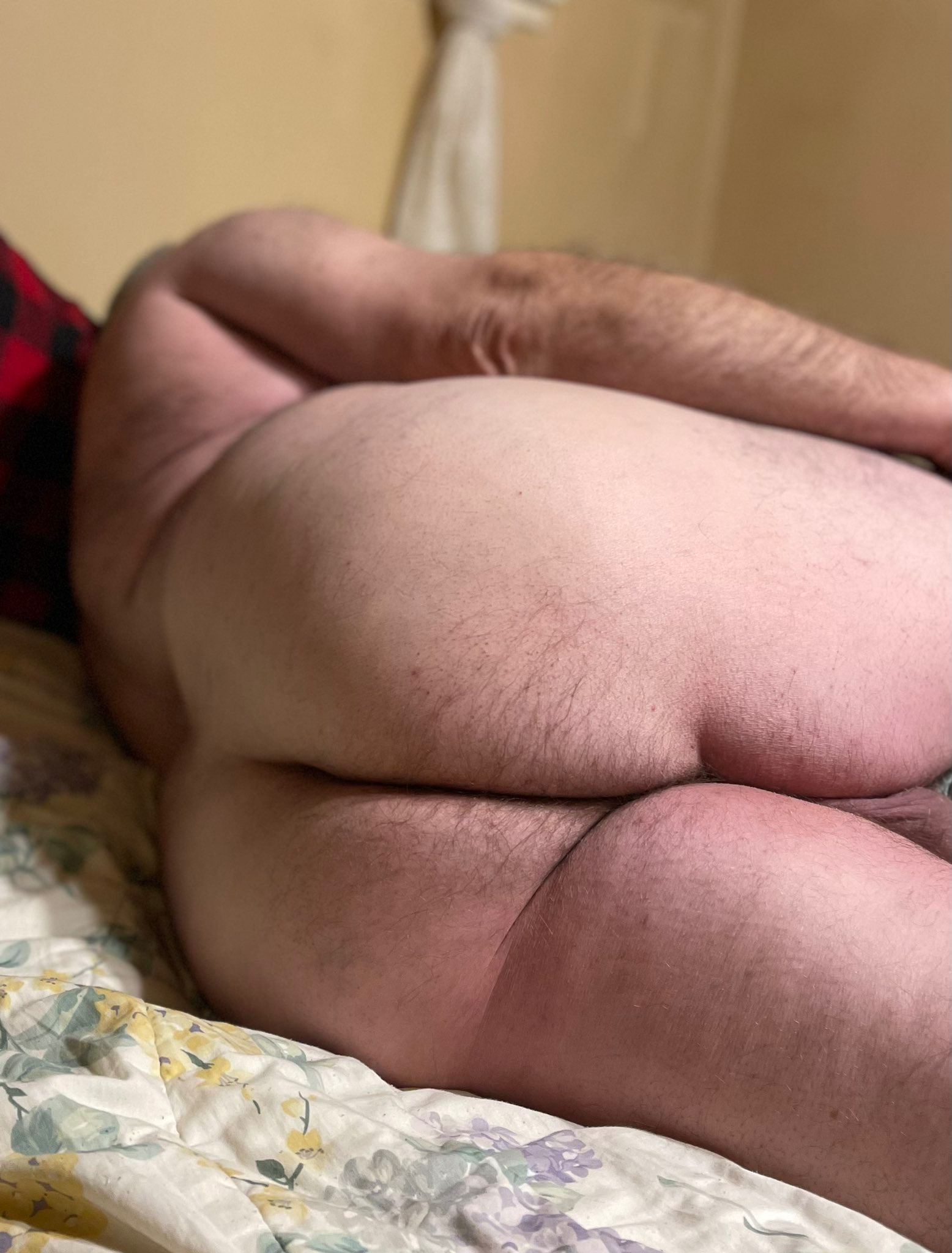 Mężczyzna leżący na łóżku w koszuli w kratę, widok z tyłu, skupiający się na pośladkach.