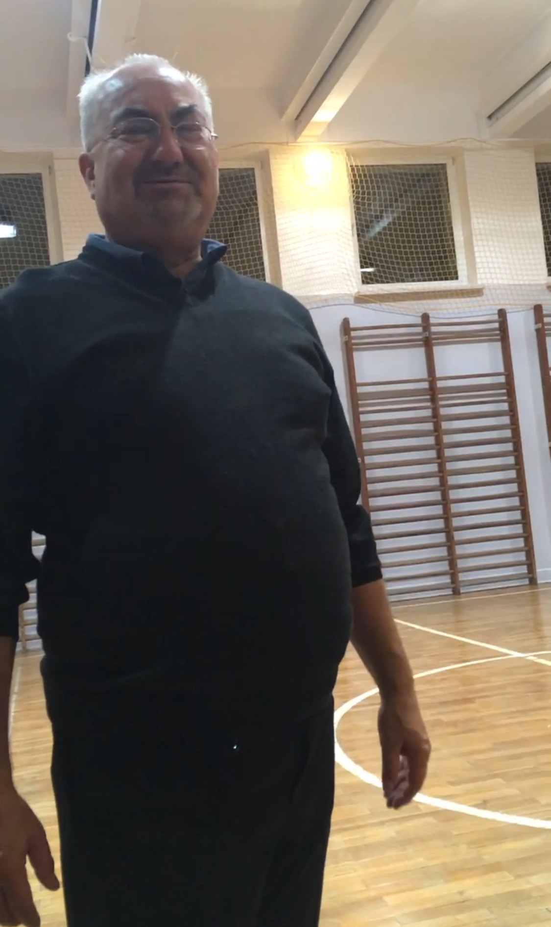 Portret mężczyzny w okularach na sali gimnastycznej w Tarnowie, z drabinkami gimnastycznymi w tle.