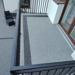 REMO-POS Damian Ostrowski - Szary balkon z żywicy epoksydowej z ciemnymi pasami dekoracyjnymi, widok z góry na reling, z meblami ogrodowymi w tle.