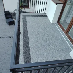 Szary balkon z żywicy epoksydowej z ciemnymi pasami dekoracyjnymi, widok z góry na reling, z meblami ogrodowymi w tle.