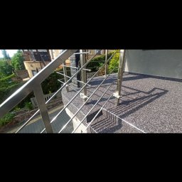 REMO-POS Damian Ostrowski - Wykończony taras z szarą, kamienną posadzką i metalową balustradą, widok z góry na fragment balkonu z widocznymi cieniami balustrady.