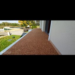 REMO-POS Damian Ostrowski - Balkon z brązową posadzką żywiczną, widok z góry na zewnątrz, z elementami zieleni w tle.