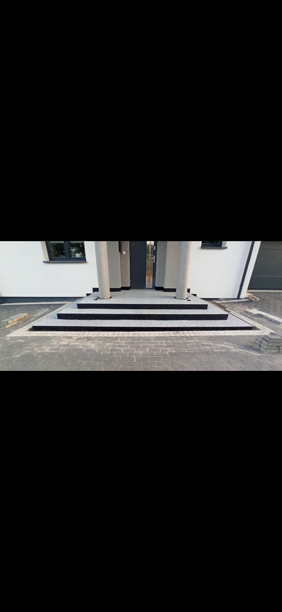 Nowoczesne schody wejściowe z szarego kamienia prowadzące do domu z białymi ścianami i kolumnami, z widoczną kostką brukową na podjeździe.