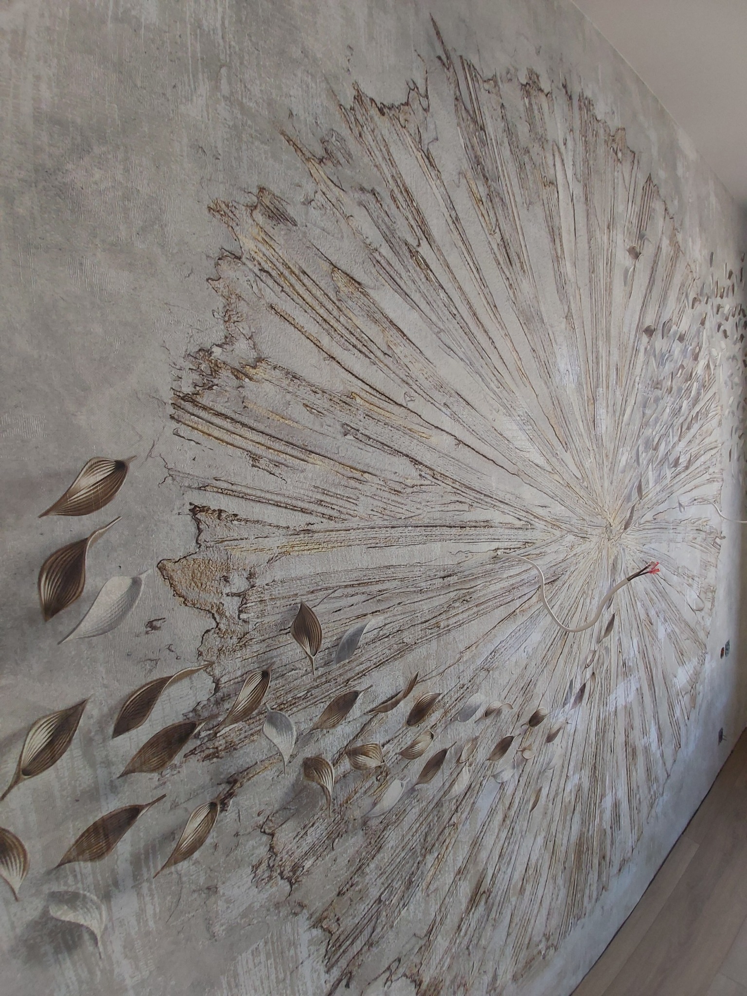 Ściana z dekoracyjną fakturą przypominającą wybuch słońca i opadające liście, widoczne przewody elektryczne.