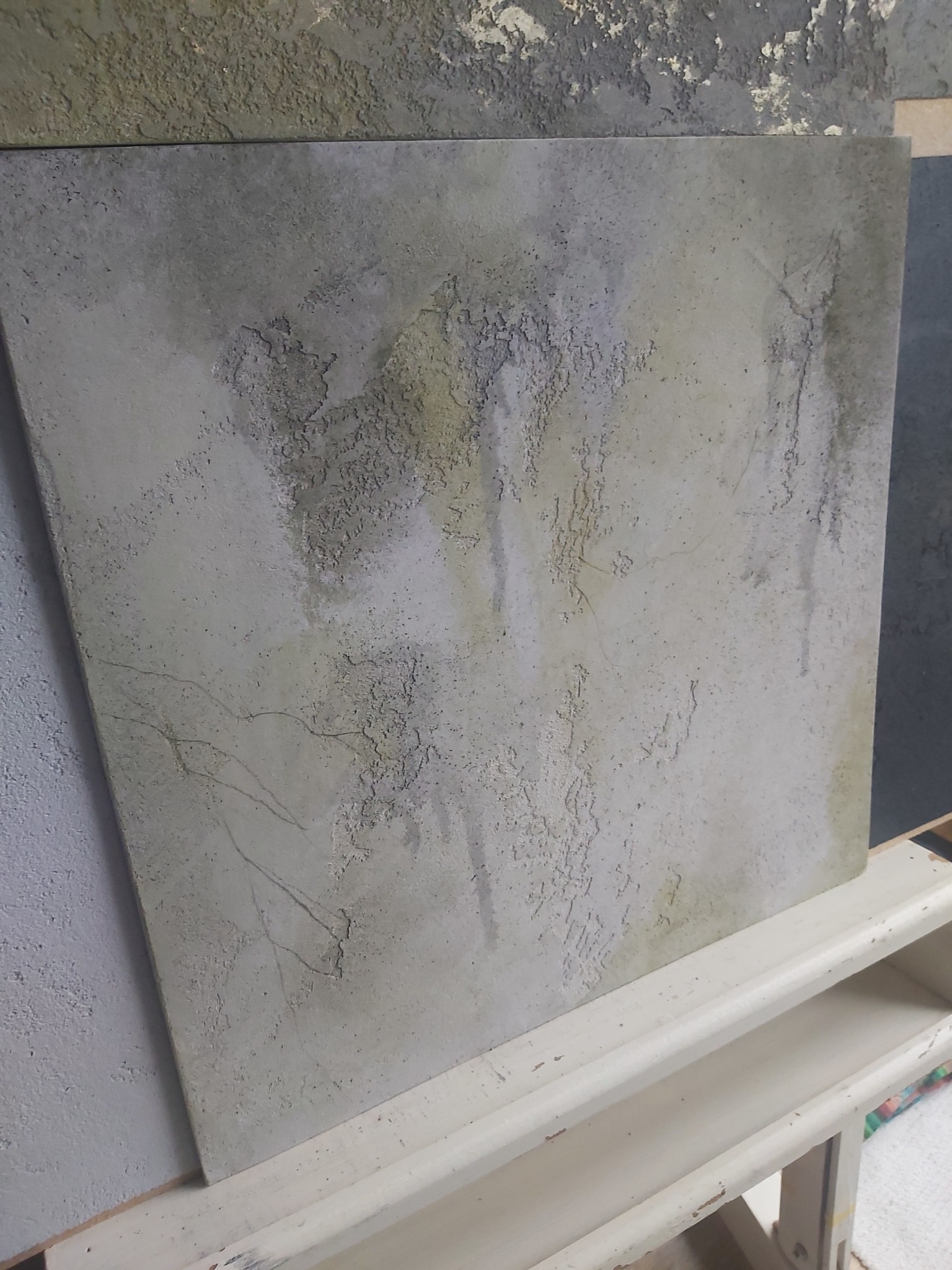 Szara płyta z efektem betonu architektonicznego, z widocznymi nieregularnymi wzorami i przetarciami, ustawiona na białym regale.